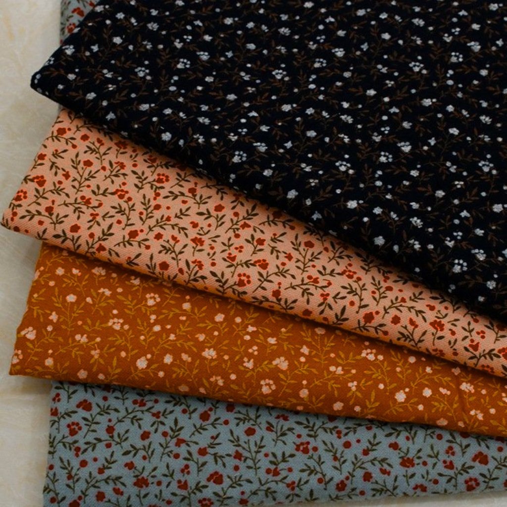 A stack of four folded floral-patterned fabrics in autumn colors (black with small white flowers on top, then peach with red and brown floral prints, burnt orange with pale flowers, and light blue-gray with red flowers) arranged diagonally.