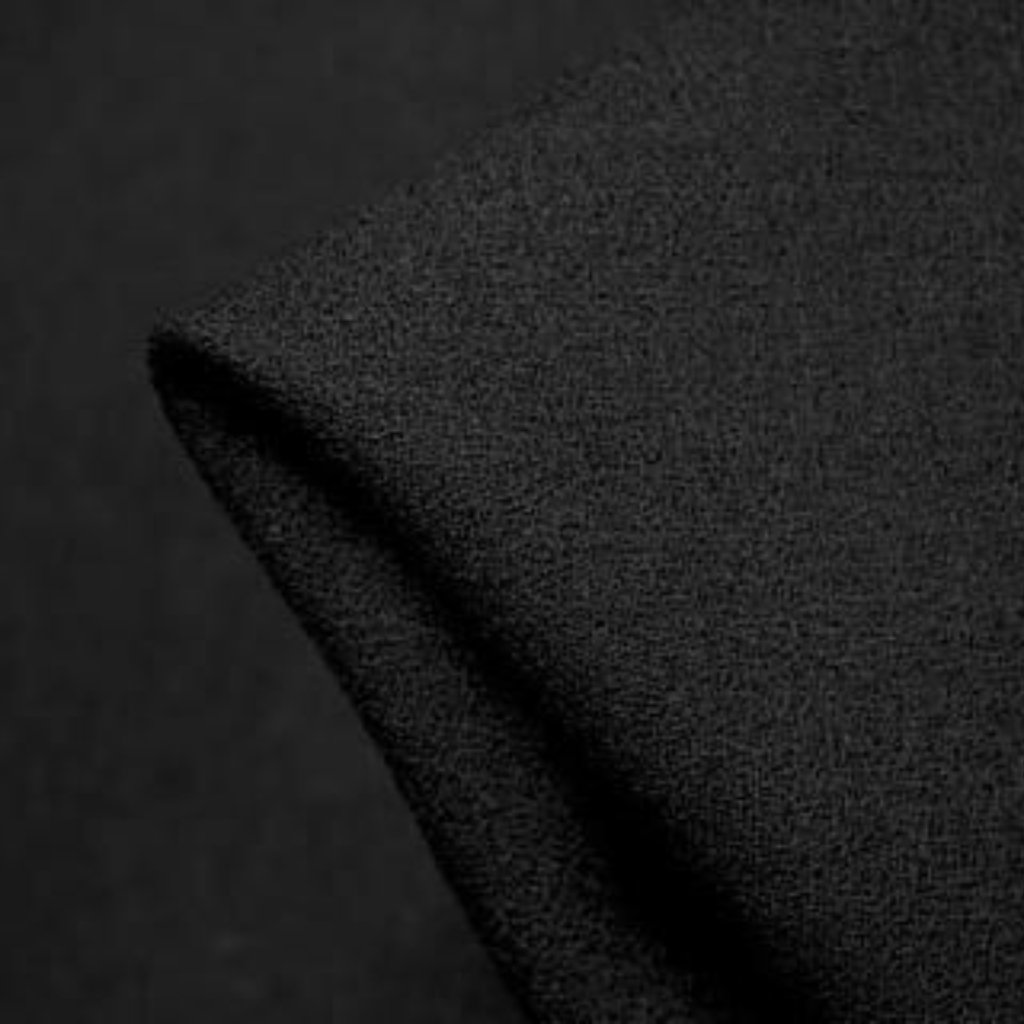 A close-up of dark black fabric with a visible seam or edge, showing a textured surface and subtle folds.