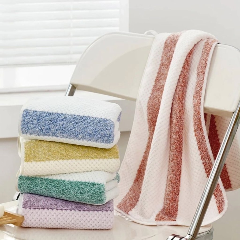 Low Pilling Polyester: A Full Guide to Smooth Durable Fabric 1 A tidy collection of folded towels in pastel colors (blue, yellow, green, lavender, white) stacked beside a chrome towel rack with a white-and-pink striped towel draped over it in a bright, clean bathroom.