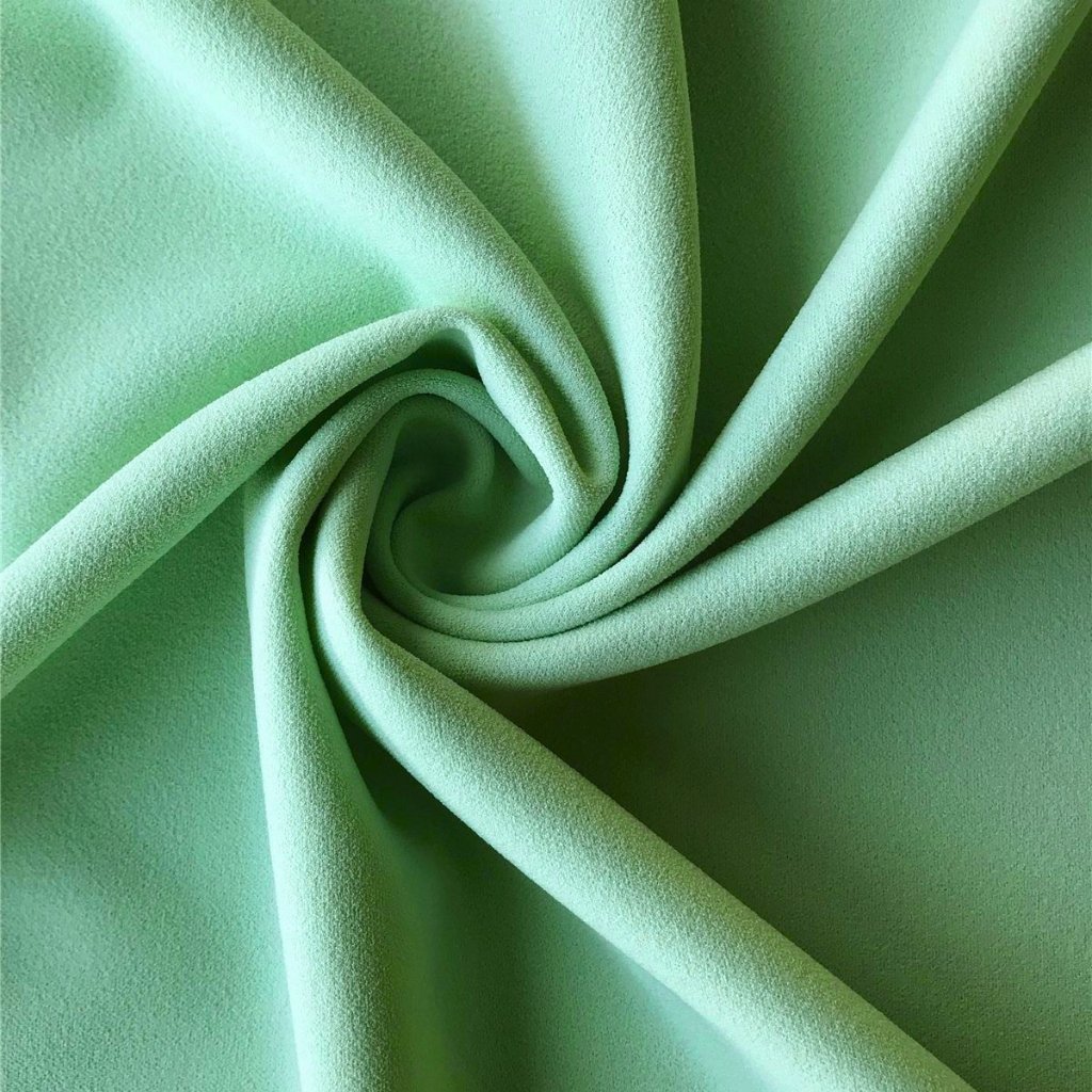 A close-up view of soft, mint-green fabric twisted into a spiral swirl, highlighting its smooth, velvety texture.