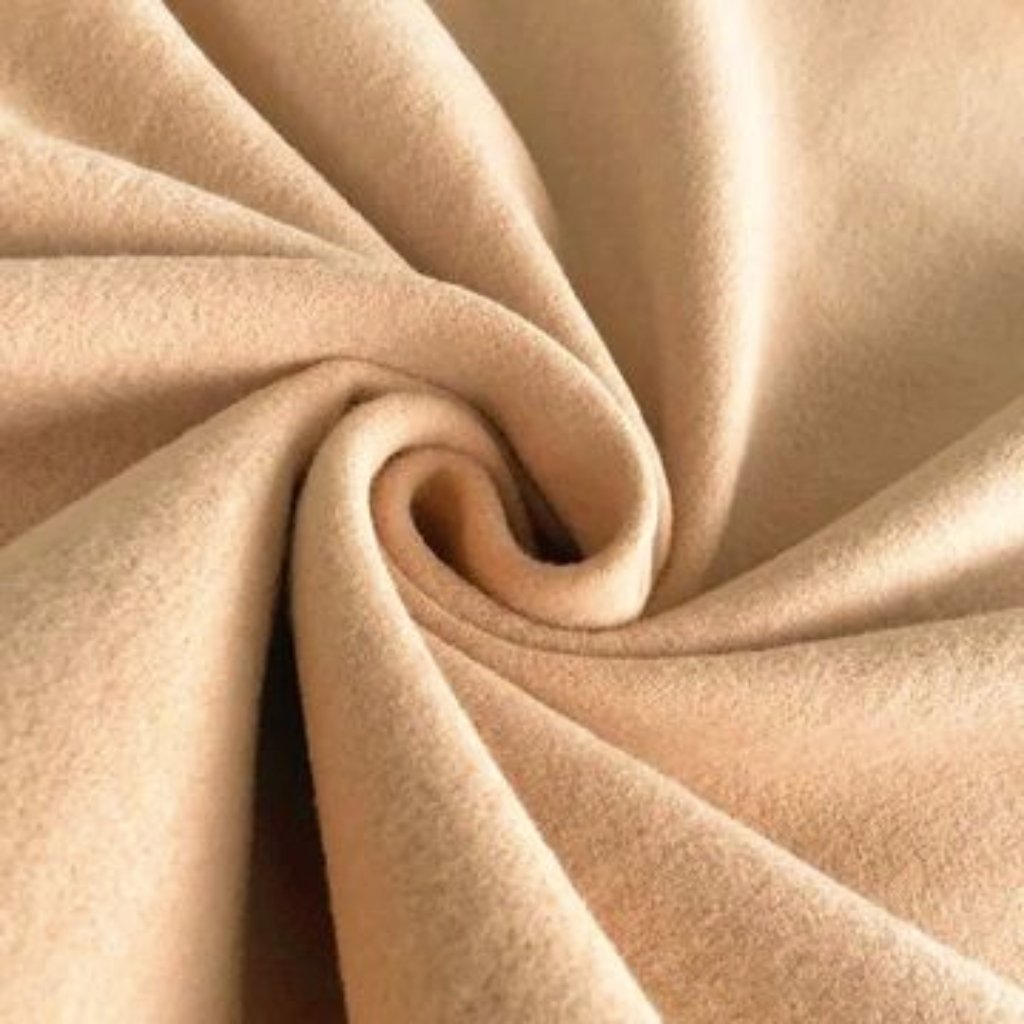 A close-up shot of soft beige suede fabric gathered into a spiral swirl, showing its smooth texture and folds.
