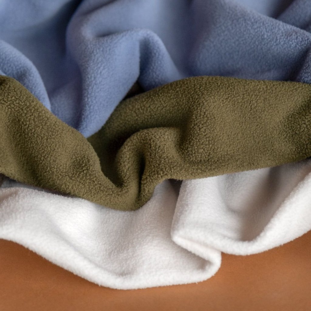 Close-up of layered, textured fleece blankets in blue, olive green, and white draped together.
