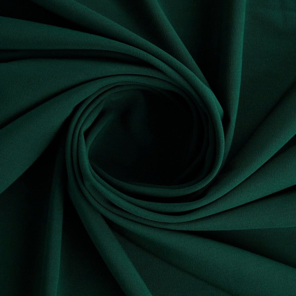 A close-up of dark emerald green fabric artistically folded into a swirl, creating soft concentric curves and shadows.