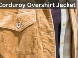 Close-up of a tan corduroy overshirt jacket with a flap pocket and button, layered over a dark knit and a plaid shirt.