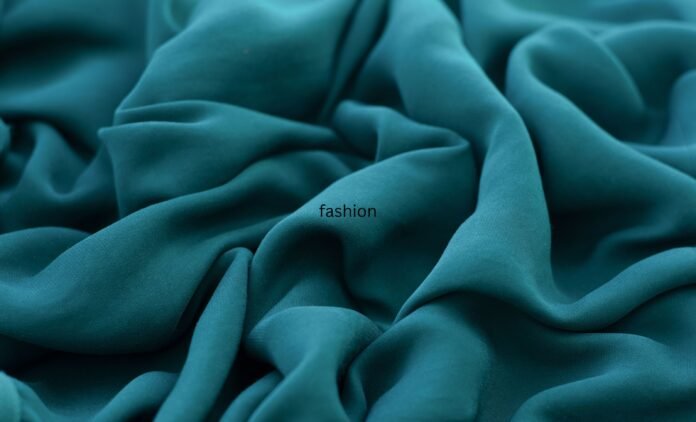 A close-up shot of luxurious teal rayon fabric with soft folds and draped waves.