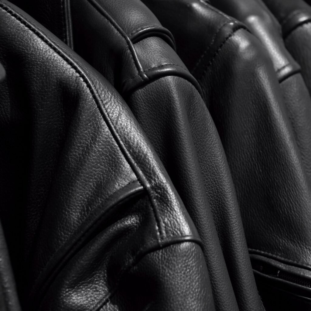 A close-up view of black leather jackets hanging or lined up, highlighting the texture and stitching of the leather.