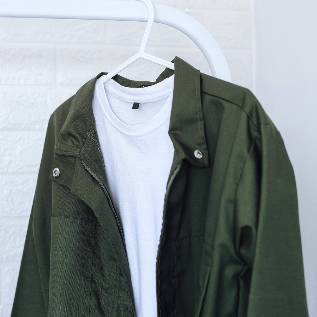 A white t-shirt layered under an olive green jacket on a white hanger against a light background.