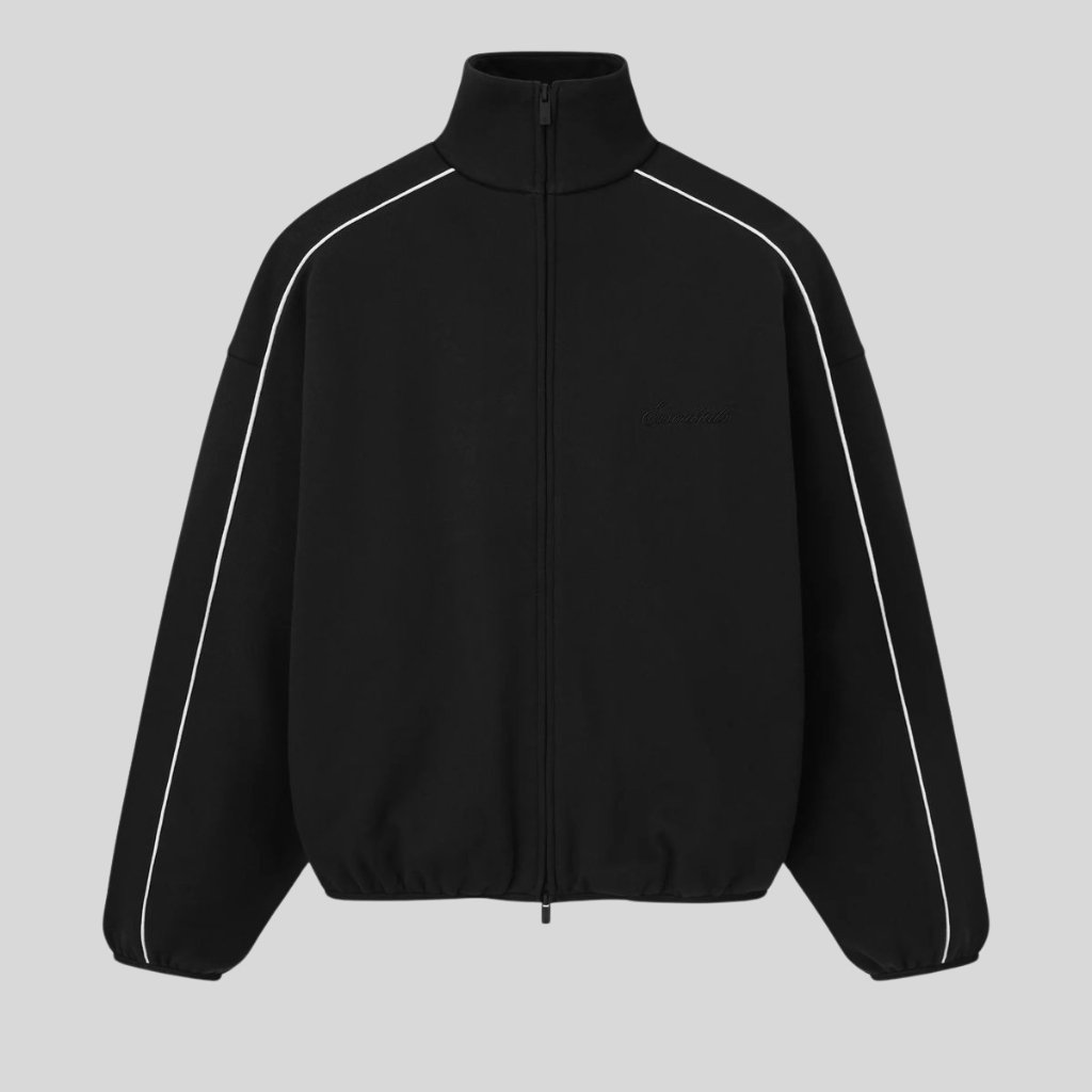 A black zip-up jacket with a high collar and white piping along the shoulders and sleeves. It has a relaxed, oversized fit with elastic cuffs and hem, and a subtle embroidery on the left chest.