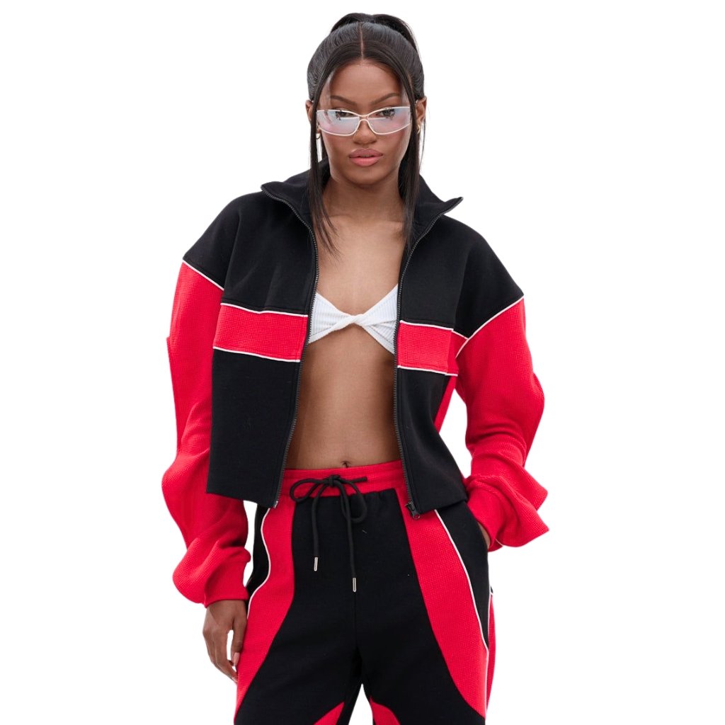 Woman wearing a black and red color-block cropped jacket with matching pants and a white twisted top, posing against a white background.