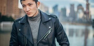 Designer Leather Jacket: Style Crafted for Modern Fashion A stylish man wearing a black leather biker jacket over a gray turtleneck, posed outdoors with a blurred cityscape in the background.