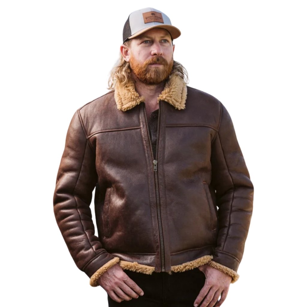 Man wearing a dark brown shearling leather coat with a tan shearling collar and cuffs, standing with hands in pockets, facing slightly left, white background.