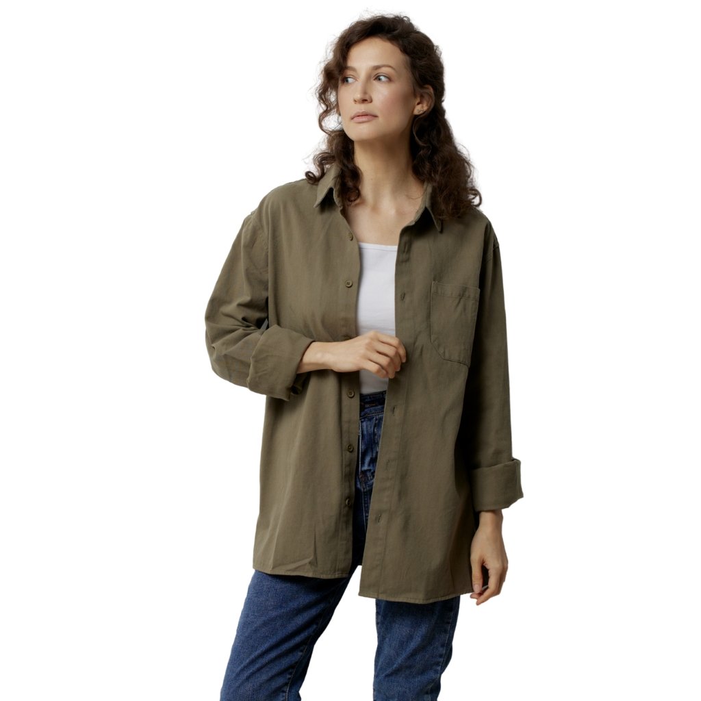 A woman wearing an oversized olive-green button-down shirt over a white top and blue jeans, looking off to the side with a neutral expression.