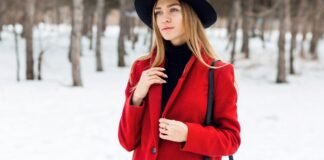 Great Coats for Winter: Classic Design Meets Modern Comfort A woman wearing a bright red coat and a black turtleneck stands in a snowy forest, holding a black strap over her shoulder and wearing a black hat. Great Coats for Winter