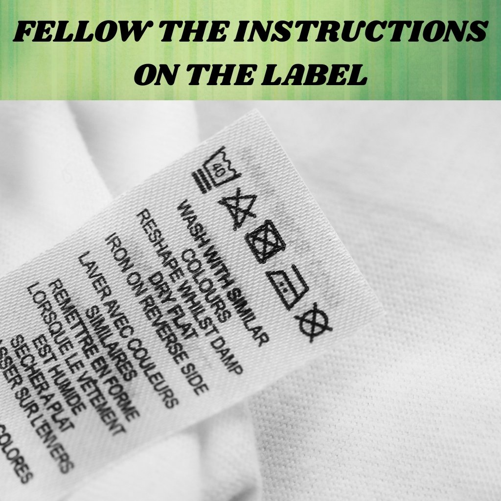 A clothing care label with washing and care icons facing upward, photographed at an angle. The label shows symbols for washing, bleaching, ironing, dry cleaning, and tumble drying, along with printed care instructions.