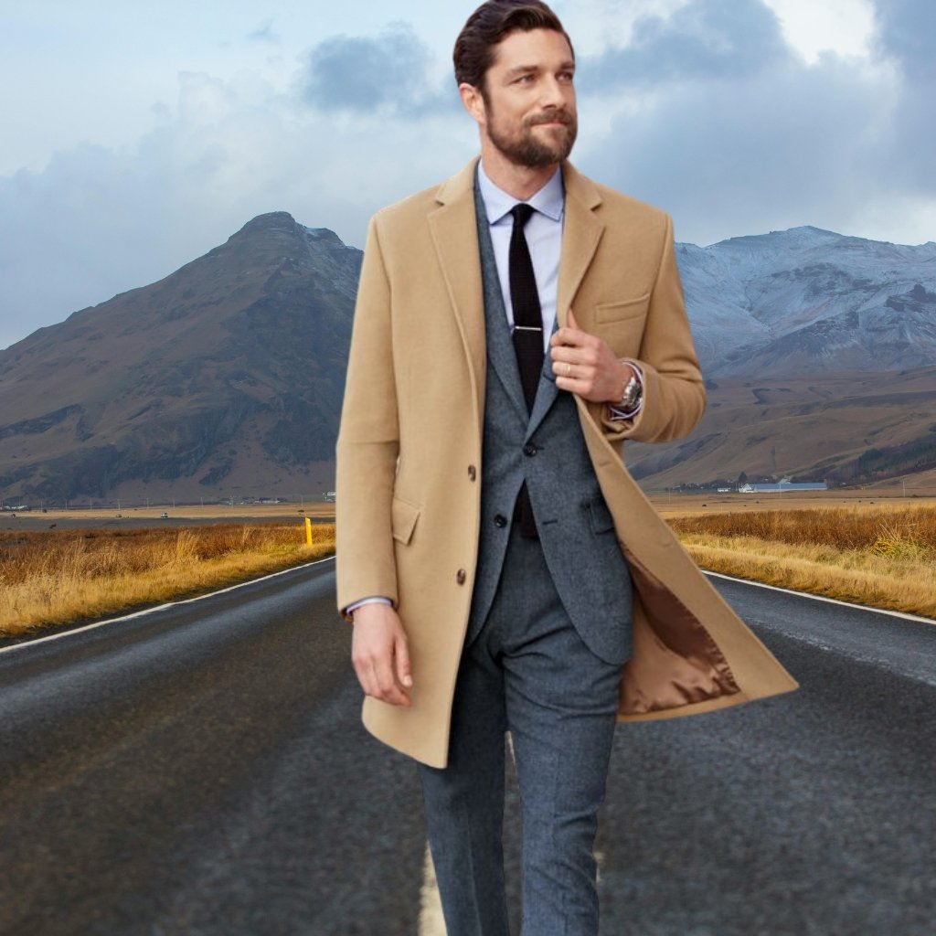 A man walking down an open rural road wearing a tan overcoat over a gray suit, with mountains in the background.