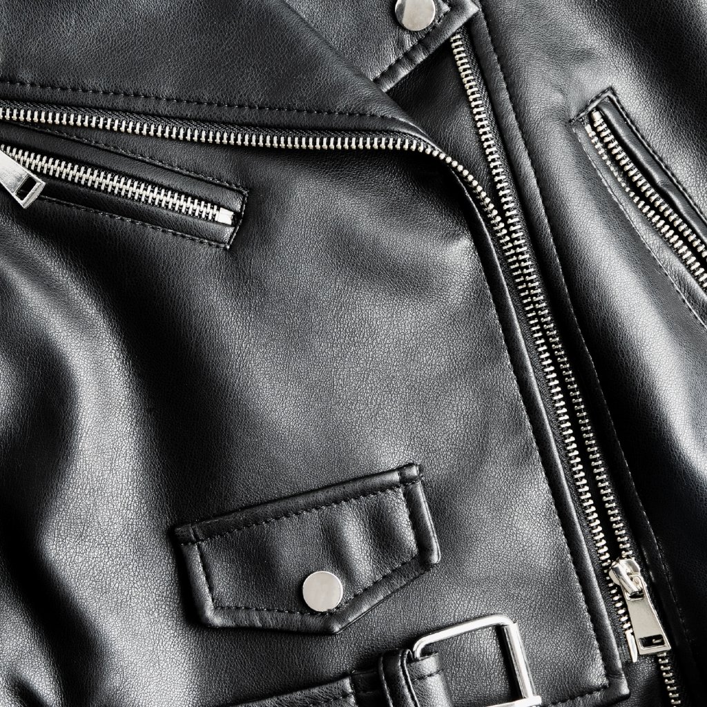 Close-up view of a black leather jacket showing metal zippers, stitching, and a small snap-tab pocket.