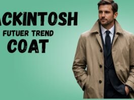 A stylish man wearing a tan Mackintosh future trend coat over a dark suit and tie, standing against a green gradient background.