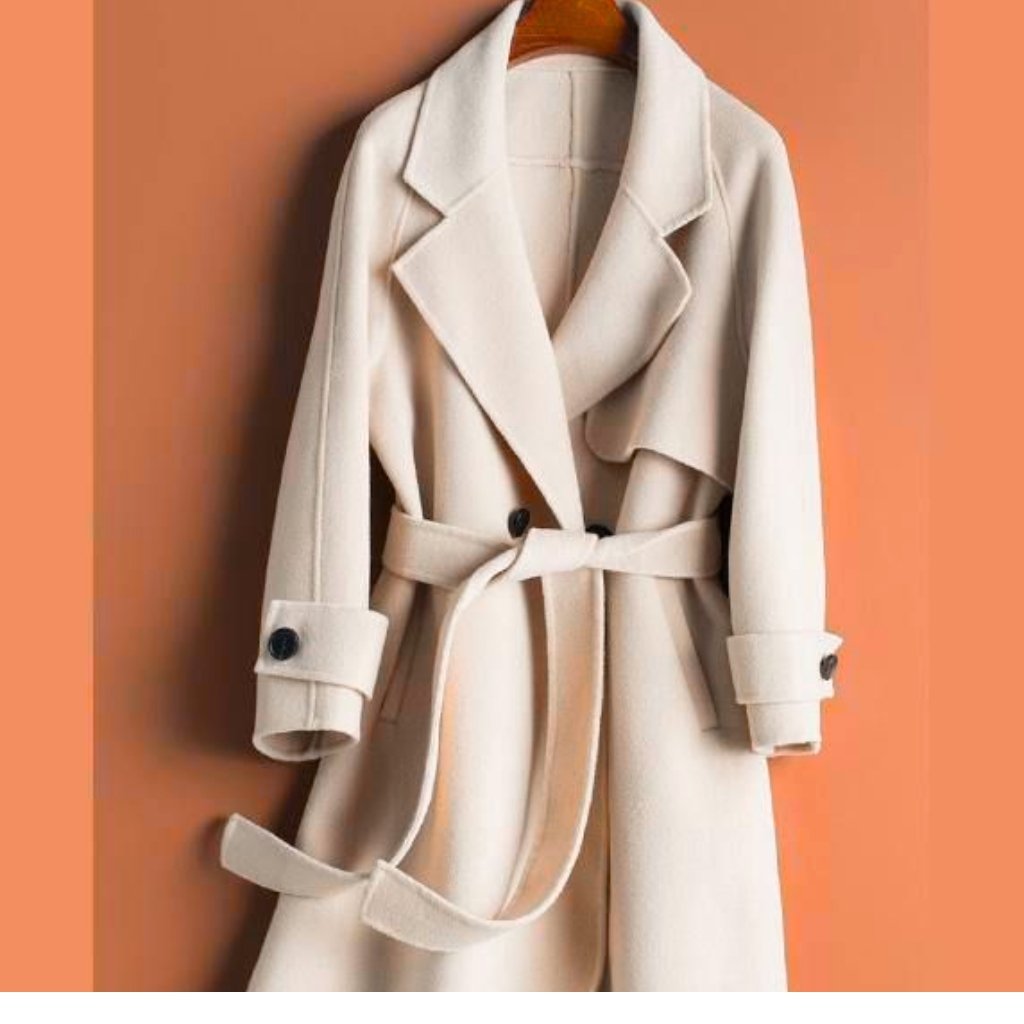 A light beige trench coat hanging on a wooden hanger against an orange background.
