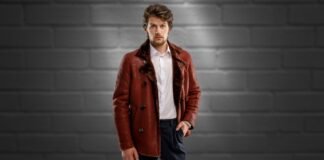 Men’s Premium Shearling Leather Coat Warmth & Style A stylish man stands against a dark brick wall, wearing a rich brown shearling leather coat, white shirt, and dark trousers.
