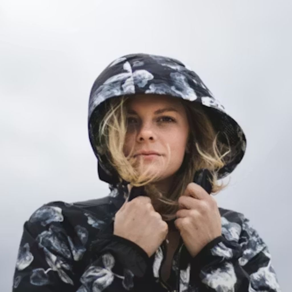 Person wearing a dark hooded jacket with a floral pattern, holding the hood closed against a light, overcast sky.Military-Inspired Winter Jackets