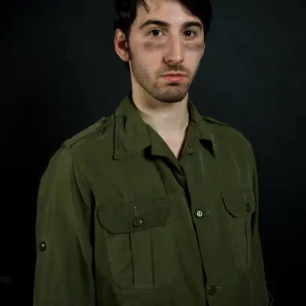 Young man wearing an olive-green military-style jacket with chest pockets, standing against a dark background.Military-Inspired Winter Jackets (5)