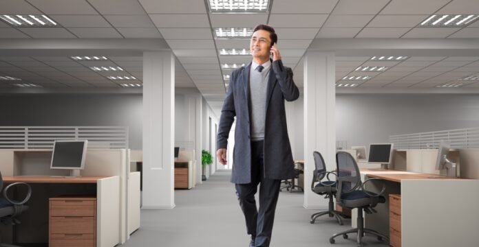 A man in a long coat walks through an empty office while talking on a mobile phone. Modern Slim Topcoat