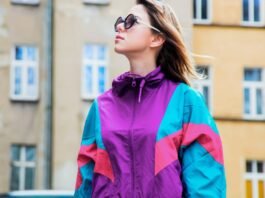 A woman wearing a colorful retro windbreaker (purple, teal, pink) and sunglasses stands outdoors in front of a beige building. Oversized Track Jacket Women