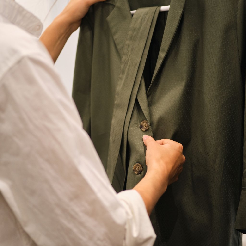  A person in a white shirt adjusting the buttons of a dark green blazer on a clothing rack, focusing on the front buttons.