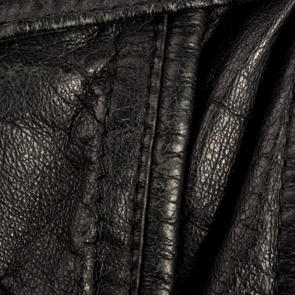 Close-up of black leather with pronounced grain and creases, showing a folded seam and smooth, reflective surface.