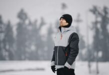 Military-Inspired Winter Jackets: Timeless Style Guide 2025 Man wearing a gray and black insulated winter jacket standing outdoors in a snowy landscape.Military-Inspired Winter Jackets