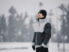 Man wearing a gray and black insulated winter jacket standing outdoors in a snowy landscape.Military-Inspired Winter Jackets