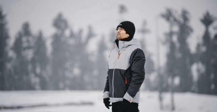 Man wearing a gray and black insulated winter jacket standing outdoors in a snowy landscape.Military-Inspired Winter Jackets