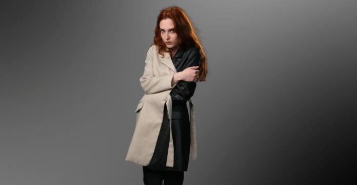 Woman wearing a beige and black color-block coat with leather sleeve against a grey background.Is a Long Parka Coat Worth It?