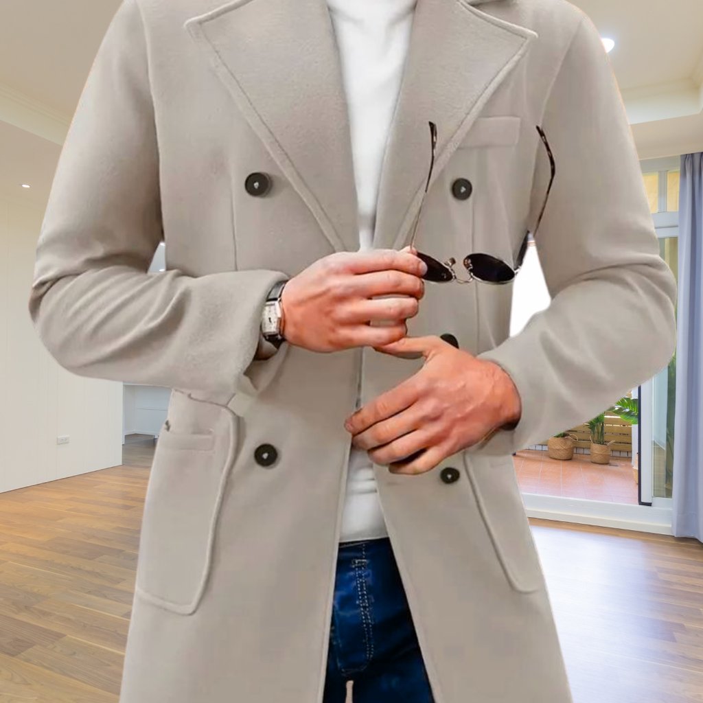 A person wearing a light gray double-breasted coat indoors, holding a pair of sunglasses in one hand and a wristwatch visible on the other wrist.
