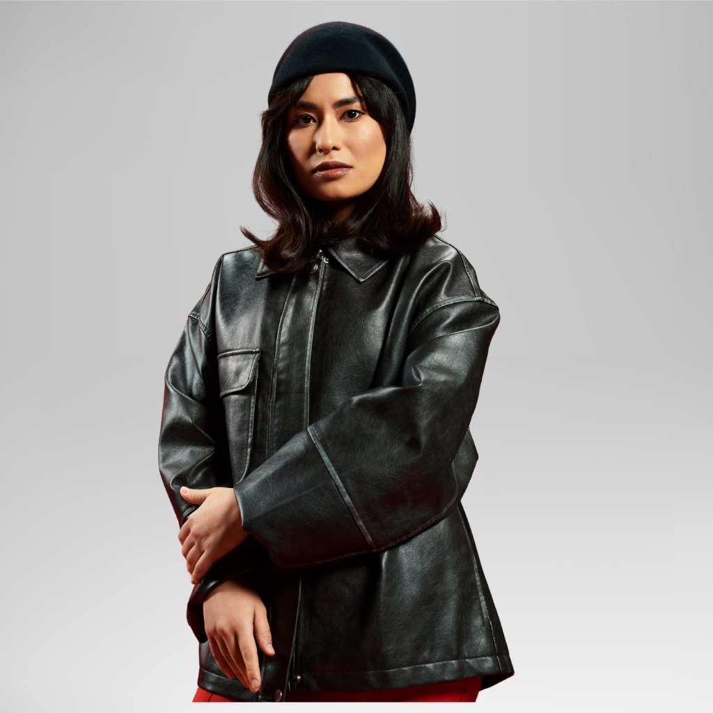 Woman wearing a sleek black longline leather jacket with oversized sleeves, paired with a black beret against a neutral backdrop.