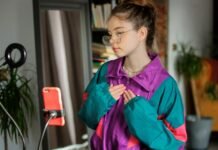 Styling Oversized Track Jacket The Ultimate Streetwear Guide A stylish young woman stands indoors in a teal, purple, and pink windbreaker, facing a smartphone on a tripod, as if recording or livestreaming. Styling Oversized Track Jacket