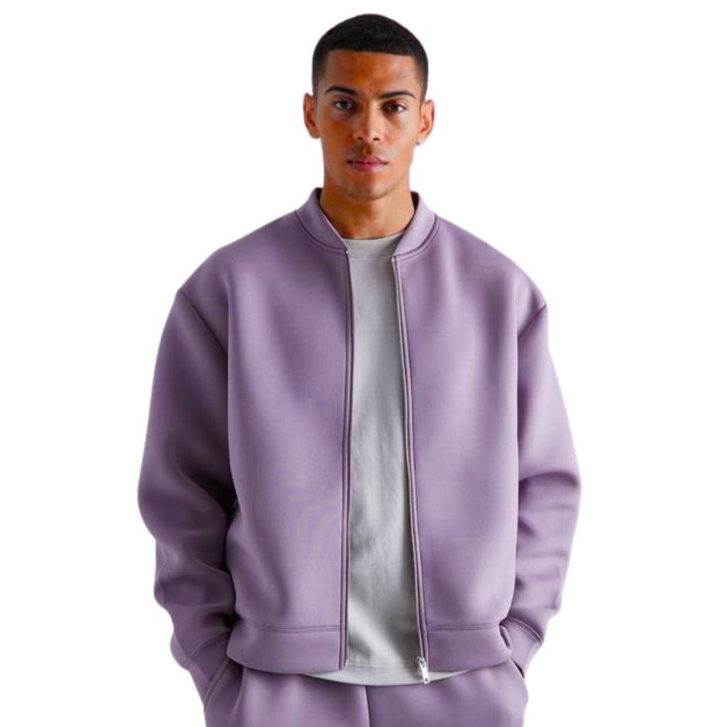 A young man stands facing the camera wearing a lilac-purple bomber jacket over a light gray T-shirt. He has short black hair and a neutral expression.