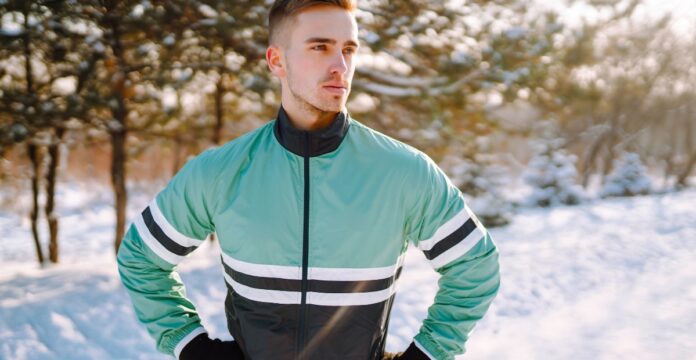 A man stands outdoors in a snowy park wearing a mint green and black windbreaker with white and black stripes across the chest and arms. Track Jacket for Men