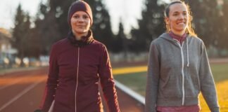 Track Jacket for Women: The Ultimate Style and Comfort Guide Two women walking on a track outdoors, one in a maroon athletic jacket with a headband and the other in a gray zip-up hoodie, smiling as they walk side by side during a sunny day. Track Jacket for Women