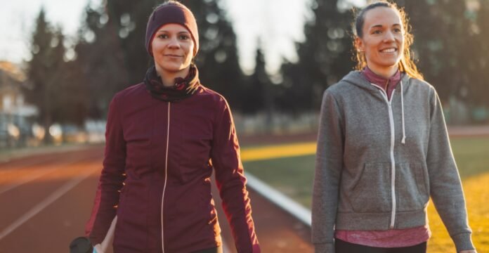 Two women walking on a track outdoors, one in a maroon athletic jacket with a headband and the other in a gray zip-up hoodie, smiling as they walk side by side during a sunny day. Track Jacket for Women