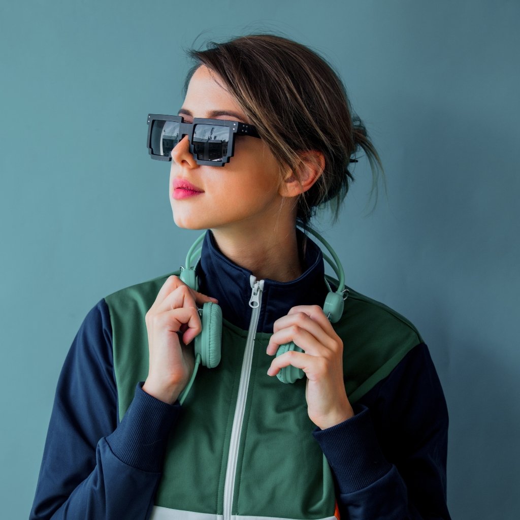 A young woman wearing oversized, square sunglasses and mint-green headphones, looking to the left with a calm expression.