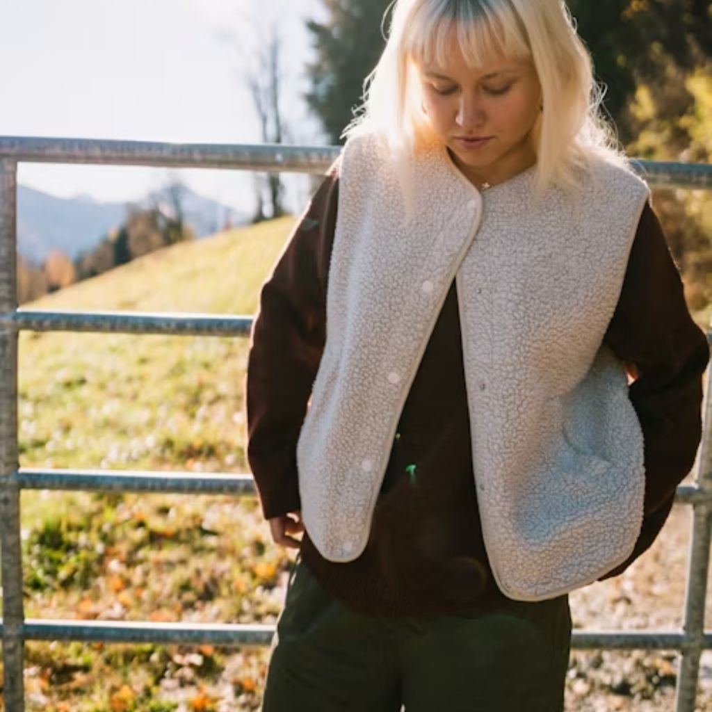 Person wearing a rust-colored jacket and holding a knitted scarf over a warm sweater in a cozy winter outfit.Boiled Wool Jacket
