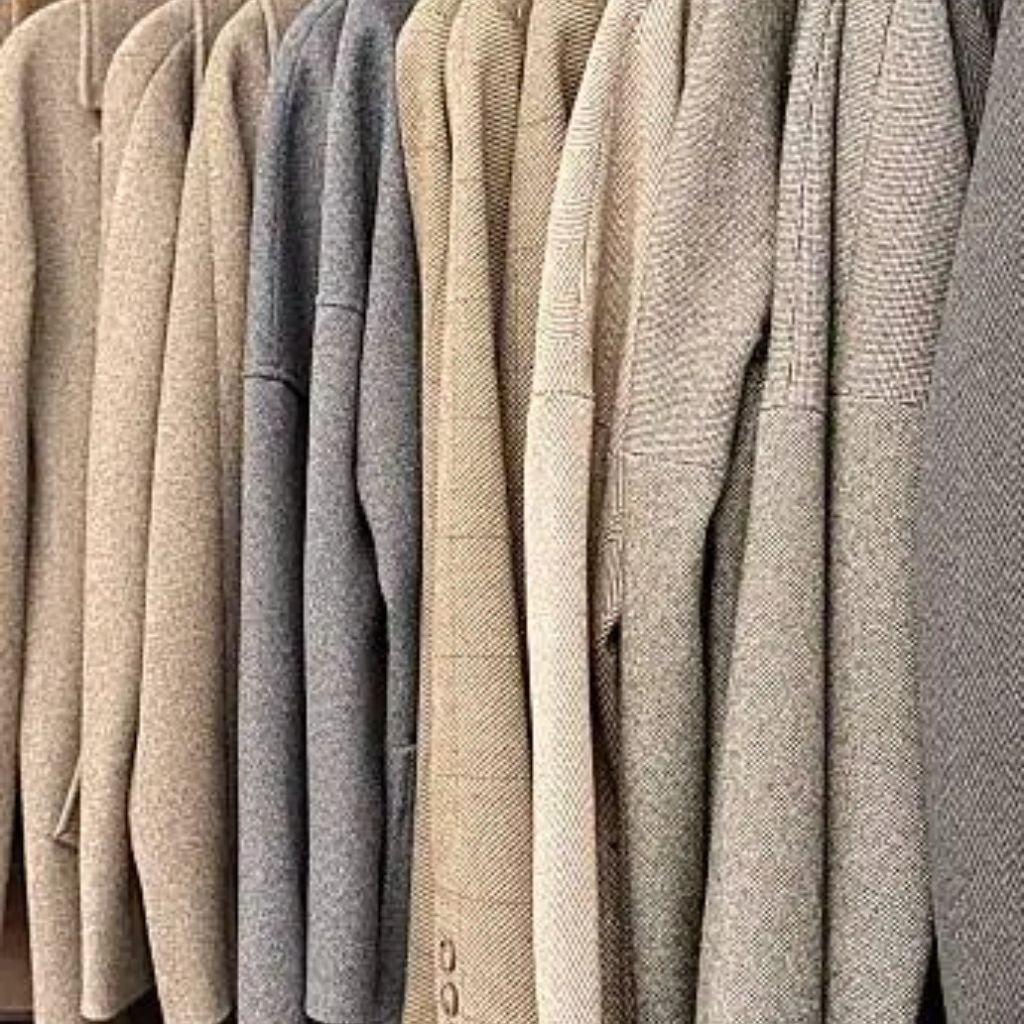 Row of neutral-toned jackets hanging side by side, showing textured fabric.Is Herringbone Wool Worth It?