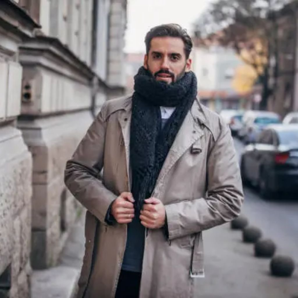 Man wearing a beige trench-style coat and black scarf standing on a city street in cool weather.Trench-Style Winter Coats