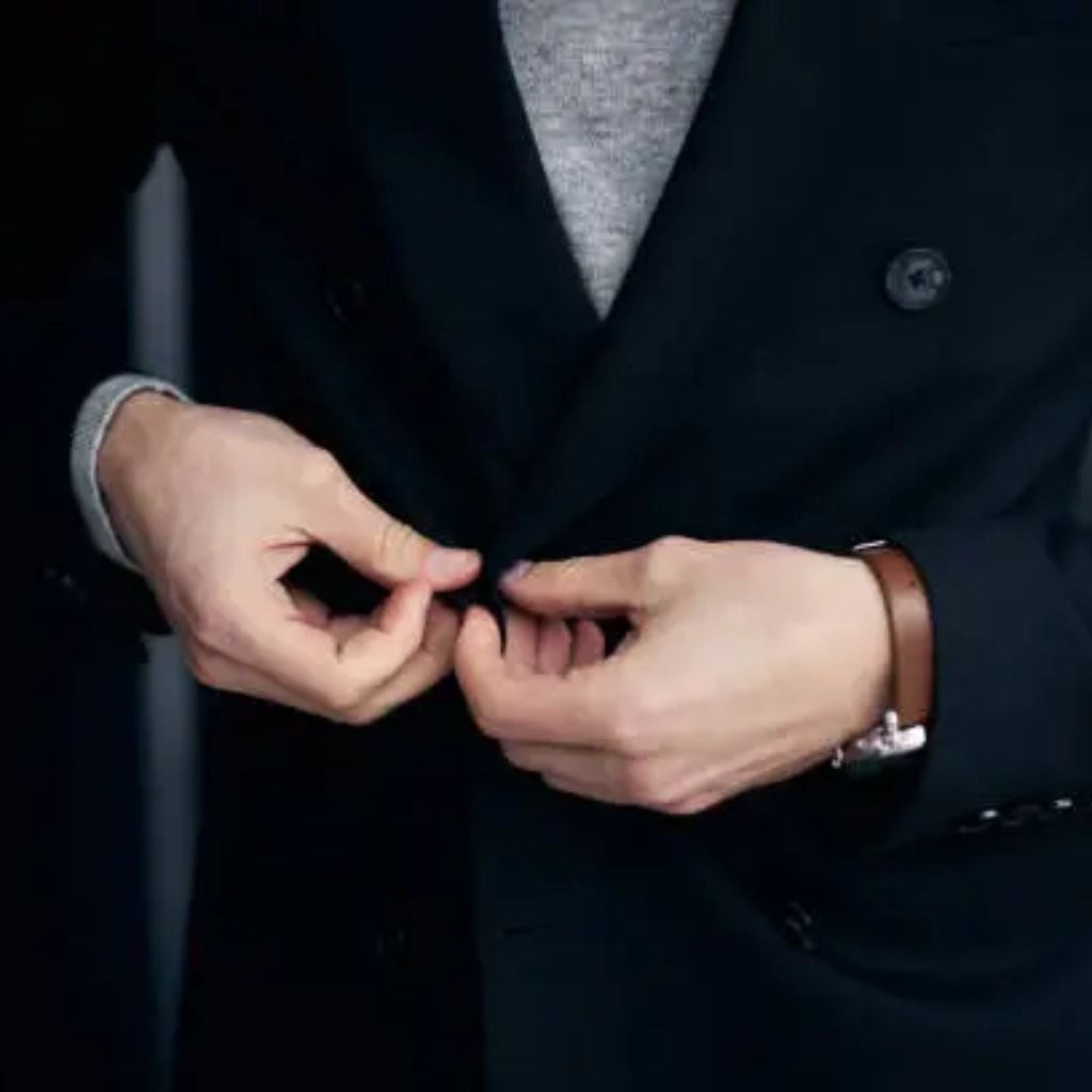Close-up of a person’s hands buttoning a dark suit jacket, with a wristwatch visible.Double-Breasted Wool Jackets: