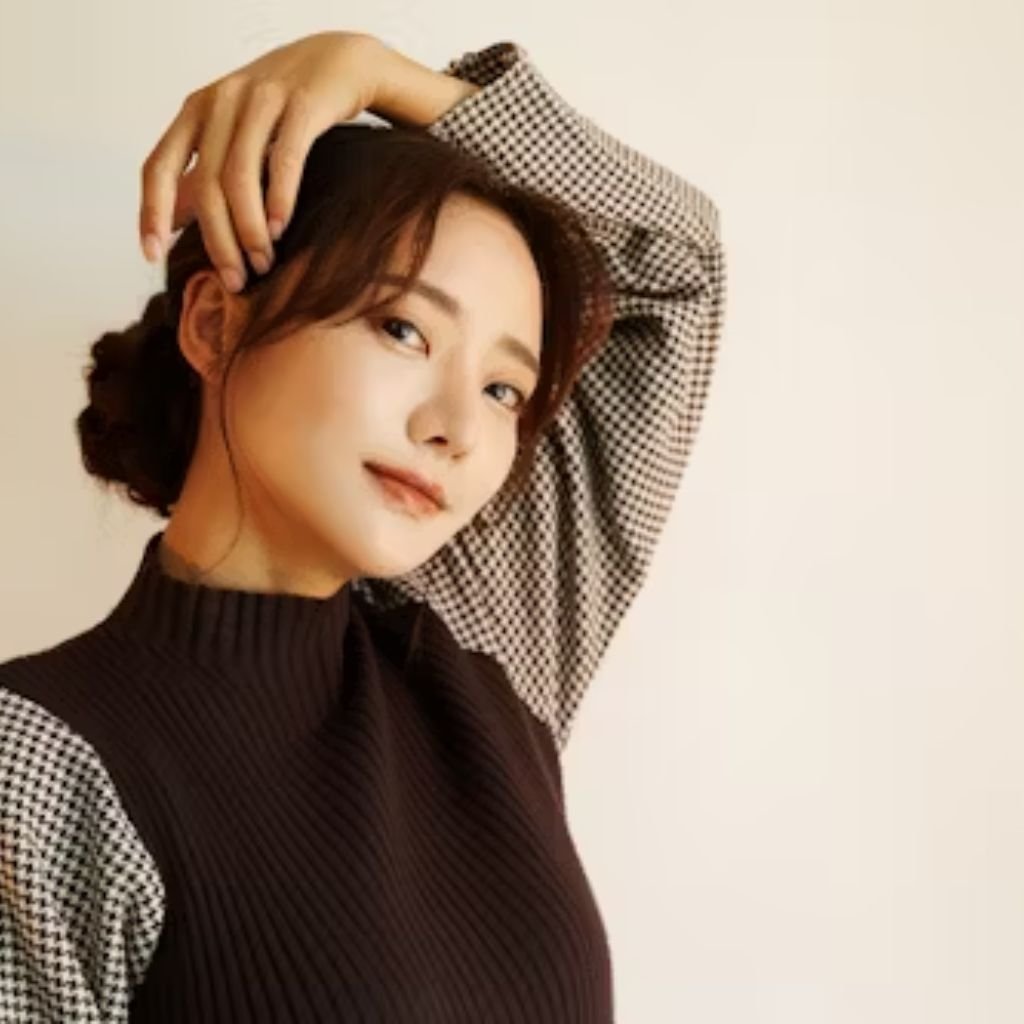 A woman posing with one hand raised over her head, wearing a dark sleeveless knit top layered over a houndstooth-patterned blouse, standing against a light background.Why Mock neck turtlenecks
