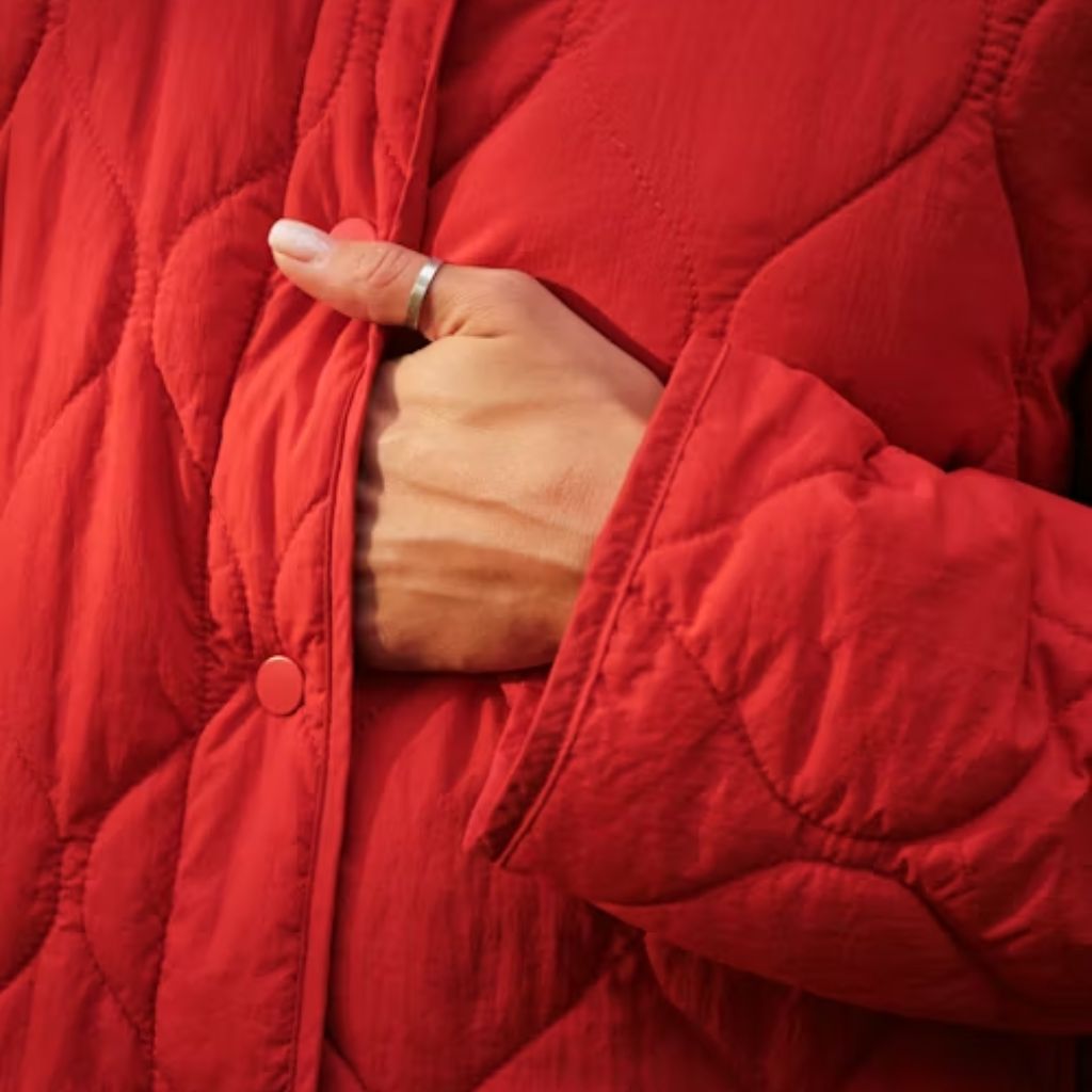 Close-up of a person wearing a red quilted jacket with one hand tucked into the pocket.Why Oversized Padded Jackets