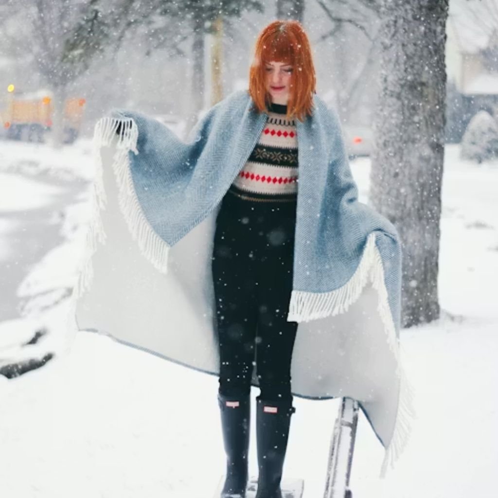 A young woman wearing a maroon sweater, black skirt, and black tights walking on a snowy path surrounded by snow-covered trees.Monochrome winter outfits