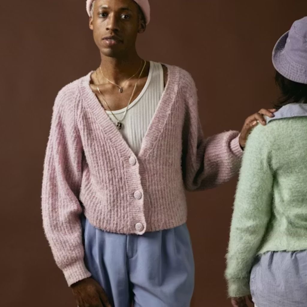 Green knitted V-neck sweater hanging on a wooden hanger against a light background with dried plants.Is Pure Wool Worth It?