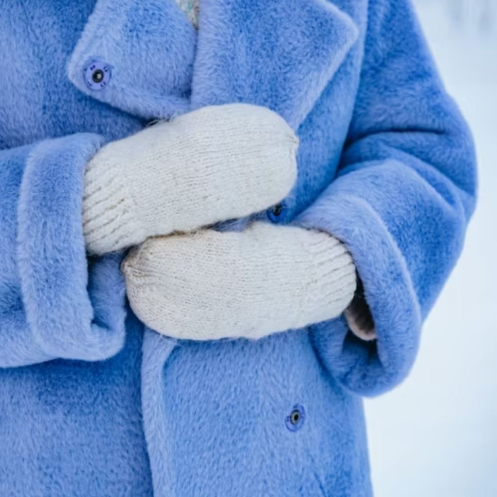 A stylish woman wearing a black long coat, white turtleneck sweater, ripped blue jeans, and a beige quilted shoulder bag with a chain strap.Why Victorian-Era Winter Coats